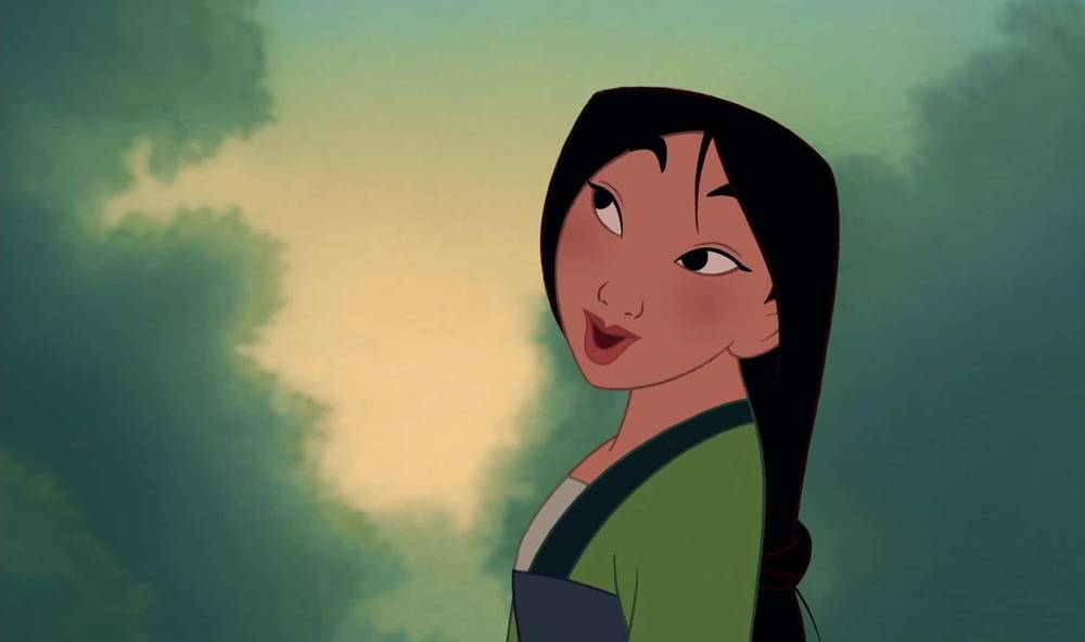 Le personnage animé de Disney, Mulan, est représenté avec une expression ludique, sur un fond vert flou. Elle a de longs cheveux noirs et porte une tenue traditionnelle bleue et verte.
