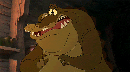 Gif animé représentant un alligator joyeux et rond battant des mains avec un large sourire dans un décor rustique faiblement éclairé, rappelant une scène de conte.
