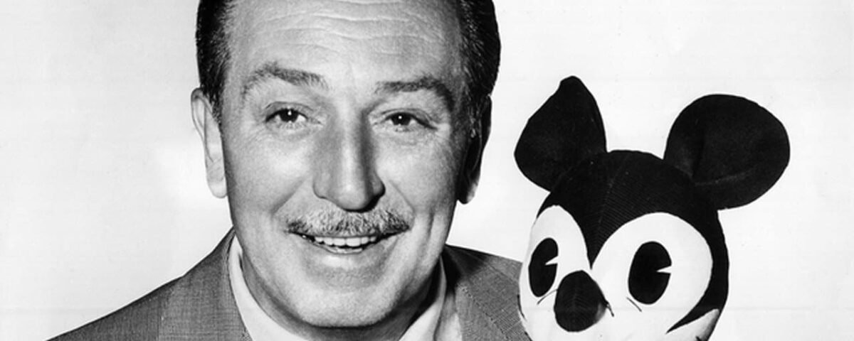 Photo en noir et blanc d'un homme souriant en costume tenant une peluche de personnage de souris de dessin animé de l'empire Walt Disney.