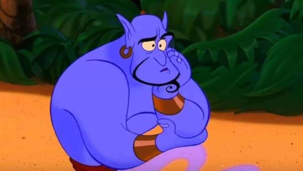 Le génie du film Disney Aladdin avec une expression triste, assis dans une zone sablonneuse avec un feuillage vert luxuriant en arrière-plan. Il a la peau bleue et les poignets jaunes.
