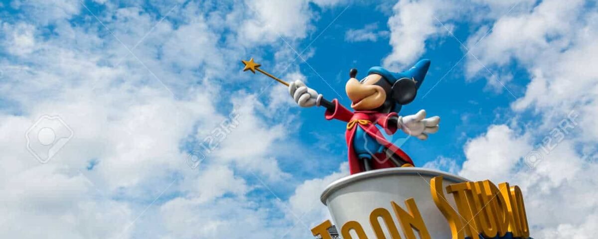 Statue de Mickey Mouse habillé en chef d'orchestre, debout sur un podium labellisé "Toon Studio", tenant une baguette, sur fond de cumulus dans un ciel bleu.