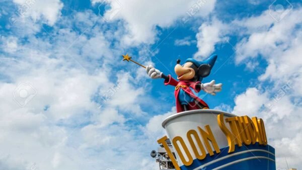 Statue de Mickey Mouse habillé en chef d'orchestre, debout sur un podium labellisé "Toon Studio", tenant une baguette, sur fond de cumulus dans un ciel bleu.
