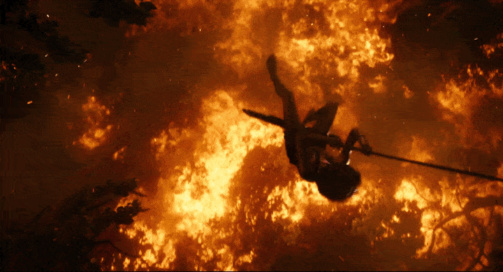 Une personne sur une tyrolienne traversant au-dessus d’intenses flammes et fumées dans un décor nocturne, évoquant une atmosphère d’aventure et de danger rappelant les scènes des contes de Rudyard Kipling.