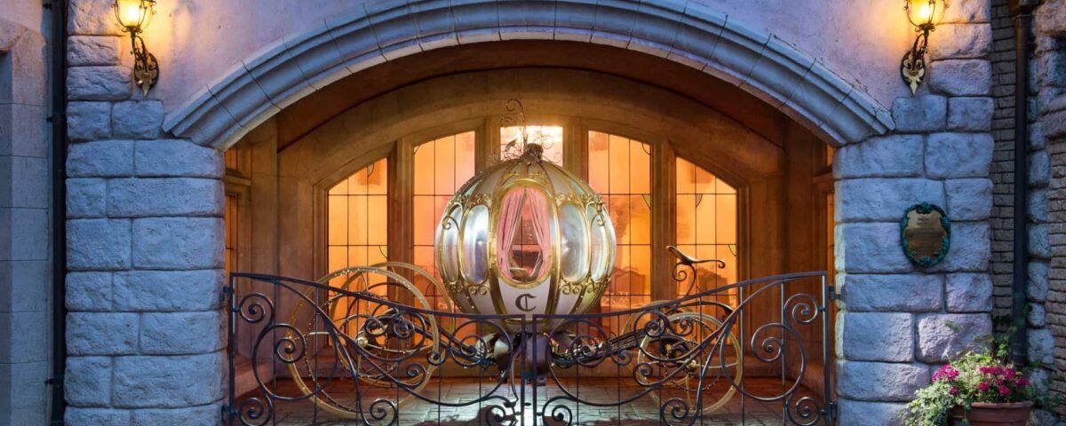 Une élégante et lumineuse calèche de style Cendrillon garée à l'intérieur d'une arcade, encadrée par des portes décoratives en fer forgé, éclairée par des lanternes au crépuscule, avec des fleurs à côté des murs en pierre, tout droit sortie d'un
