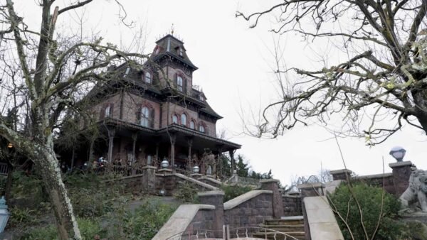 Un manoir victorien aux ornements envoûtants, inspiré du Phantom Manor de Disney, se trouve au sommet d'une colline, entouré d'arbres dénudés sous un ciel nuageux, dégageant une ambiance mystérieuse et inquiétante. Les visiteurs sont visibles