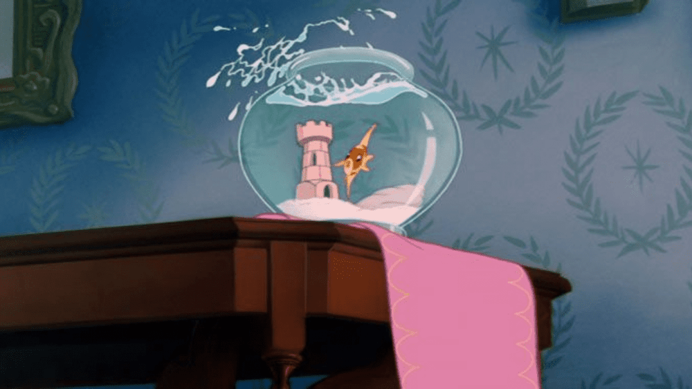 Un poisson rouge dans un bocal à poissons sur une table en bois, avec une décoration de château de style animé à l'intérieur du bol rappelant Poisson Disney, sur fond de pièce tapissée.