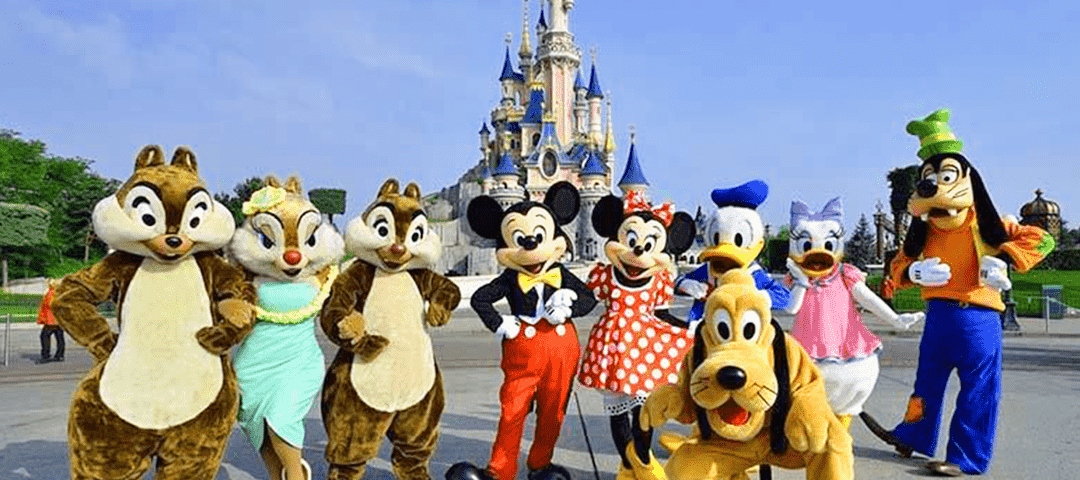 Personnages Disney costumés, dont Chip et Dale, Mickey, Minnie, Dingo, Donald Duck et Pluto, posant devant le château de Cendrillon par une journée ensoleillée.