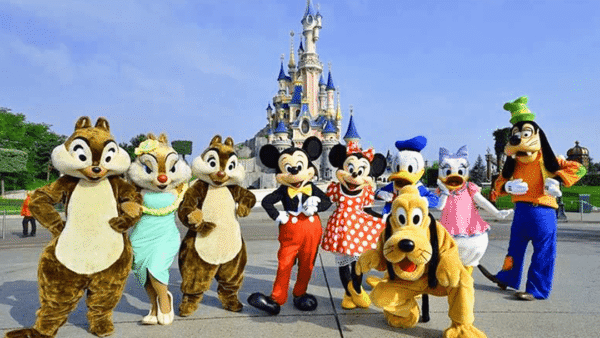 Personnages Disney costumés, dont Chip et Dale, Mickey, Minnie, Dingo, Donald Duck et Pluto, posant devant le château de Cendrillon par une journée ensoleillée.