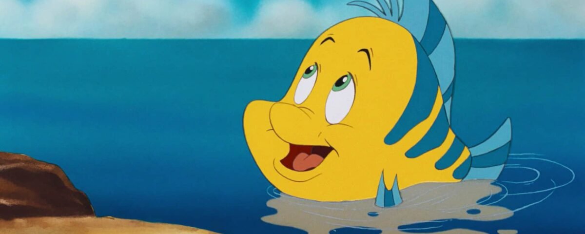 Une image de dessin animé d'un joyeux poisson rayé jaune et bleu avec une nageoire proéminente, nageant près de la surface d'une eau bleu clair, avec un fond sablonneux et des rochers visibles, qui rappelle les films de Disney.