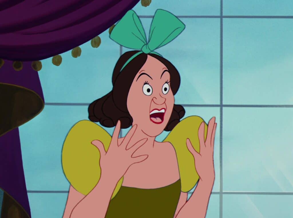 Une image animée mettant en vedette Drizella, un personnage de l'opéra Cendrillon, affichant une expression choquée avec des yeux écarquillés et des mains levées à côté de son visage. Elle porte un nœud vert et une robe jaune