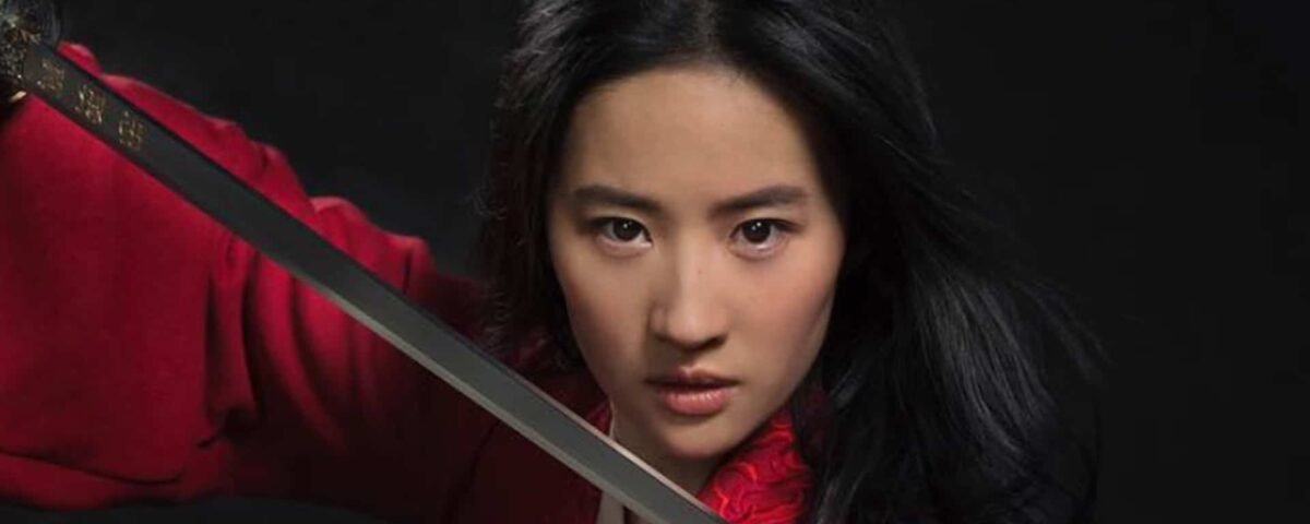 Une femme en tenue rouge, rappelant Mulan, tenant une épée pointée vers la caméra avec une expression intense. Elle a de longs cheveux noirs flottants et un air déterminé.