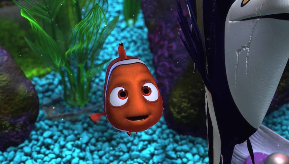 Image animée tirée des films Disney de Nemo, un poisson-clown, surpris à côté d'un poisson plus gros dans un décor sous-marin coloré avec des cailloux bleus et des plantes vertes.
