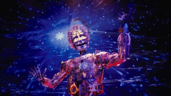 Un robot fantaisiste avec une tête en forme de dôme transparent, des fils colorés pour les cheveux et des parties mécaniques du corps, sur fond d'espace étoilé à Discoveryland, s'étendant comme s'il interagissait avec les étoiles.