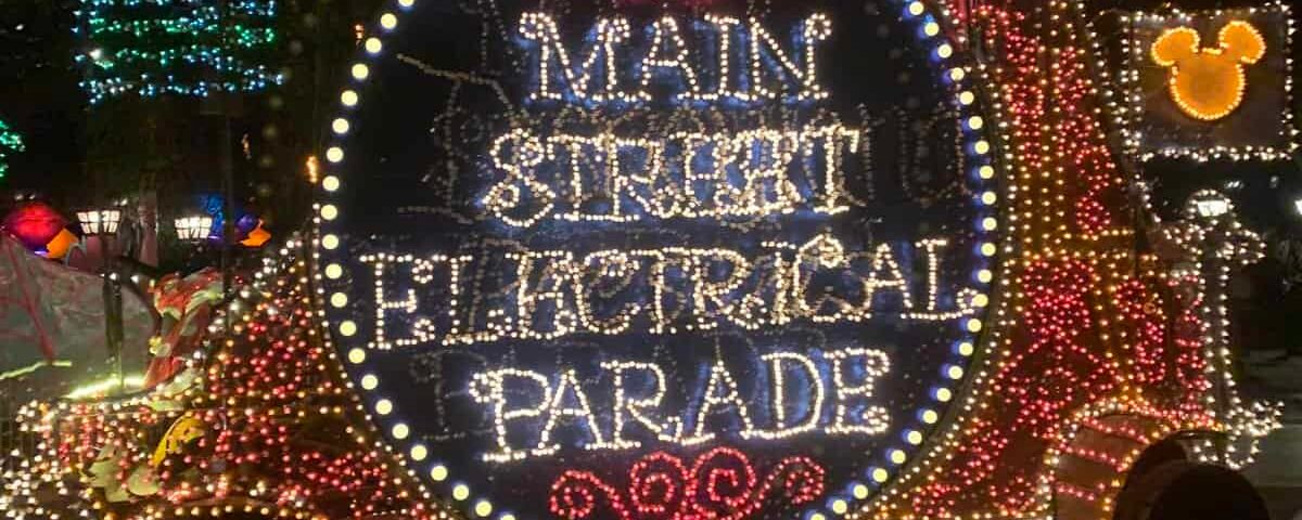 Une scène nocturne vibrante d'un char électrique de la rue principale de Disneyland, orné de lumières multicolores comportant des mots et des dessins, avec une figurine de Mickey Mouse agitant du haut.