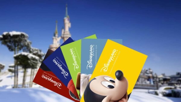 Une collection de billets colorés de Disneyland Paris représentant Mickey Mouse, affichés au premier plan avec un château Disneyland enneigé en arrière-plan sous un ciel bleu clair.