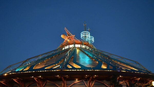 Une photo nocturne vibrante d'un manège "De la Terre à la Lune" à Disneyland Paris, mettant en vedette une structure en forme de moulin à vent illuminée de chaudes lumières orange et turquoise, sur un fond sombre