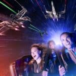 Trois personnes profitant d'une aventure spatiale dynamique en réalité virtuelle à Disneyland Paris, riant et saisissant leurs poignées alors que les vaisseaux spatiaux se battent autour d'eux sur fond d'étoiles et de faisceaux laser colorés.