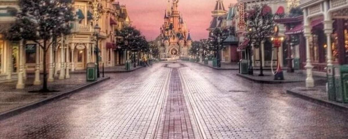 Vue tôt le matin d'une rue principale vide de Disneyland menant à l'emblématique château de la Belle au bois dormant, sous un ciel rose et violet.