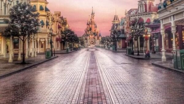Vue tôt le matin d'une rue principale vide de Disneyland menant à l'emblématique château de la Belle au bois dormant, sous un ciel rose et violet.