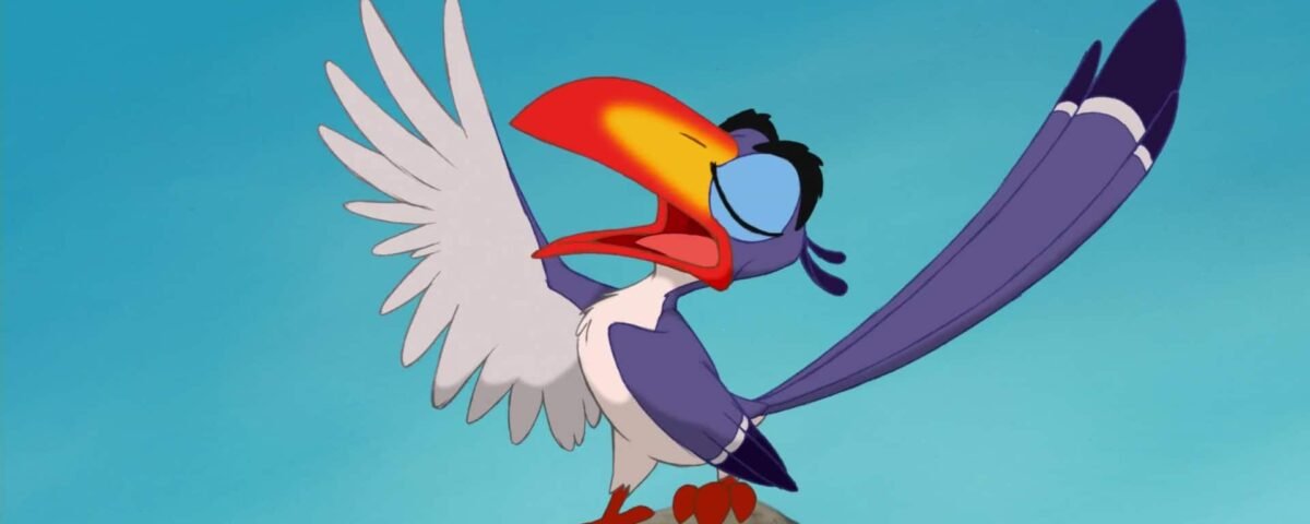 Un oiseau de dessin animé coloré avec un grand bec orange, des plumes bleues et des ailes blanches, portant des lunettes, debout sur un rocher avec ses ailes largement déployées sur un fond de ciel bleu.