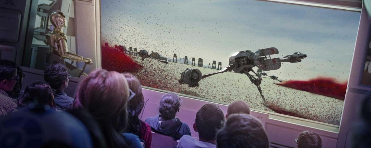 Un public captivé à bord d'un vaisseau spatial regarde un grand écran montrant une scène de robots marcheurs sur un paysage aride et rocheux, qui rappelle l'attraction Star Tours de Disneyland Paris.