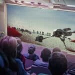 Un public captivé à bord d'un vaisseau spatial regarde un grand écran montrant une scène de robots marcheurs sur un paysage aride et rocheux, qui rappelle l'attraction Star Tours de Disneyland Paris.
