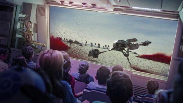 Un public captivé à bord d'un vaisseau spatial regarde un grand écran montrant une scène de robots marcheurs sur un paysage aride et rocheux, qui rappelle l'attraction Star Tours de Disneyland Paris.