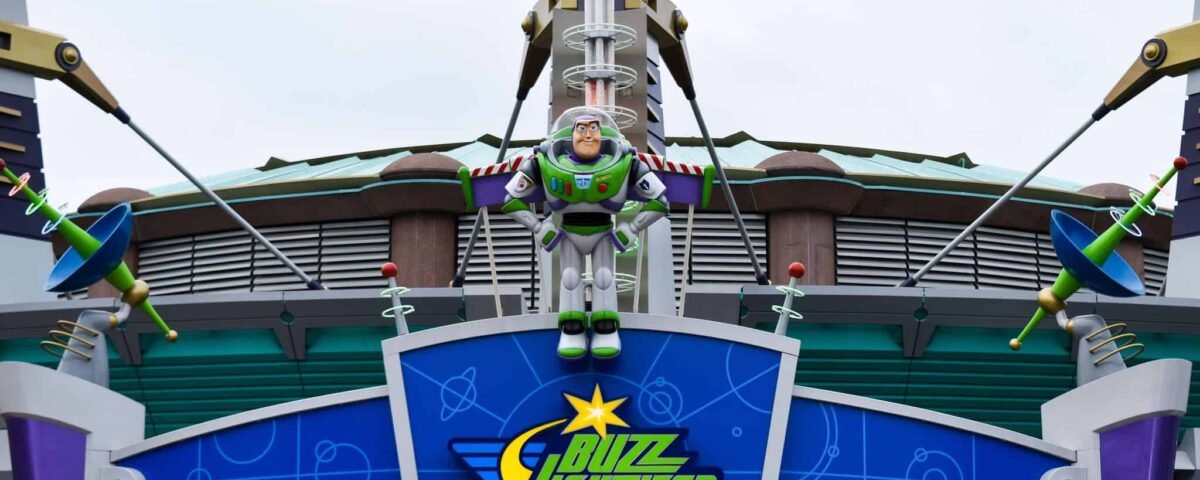 Une entrée colorée à Discoveryland pour le manège Buzz Lightyear Laser Blast avec une grande figure de Buzz l'Éclair au centre, flanquée de petites figures extraterrestres vertes, sous un ciel nuageux.