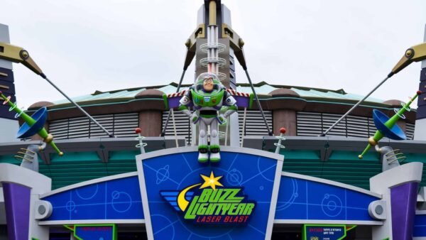 Une entrée colorée à Discoveryland pour le manège Buzz Lightyear Laser Blast avec une grande figure de Buzz l'Éclair au centre, flanquée de petites figures extraterrestres vertes, sous un ciel nuageux.