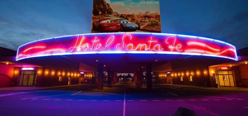 L'image montre l'enseigne au néon très éclairée de « l'Hôtel Santa Fe » à Disneyland Paris. Le panneau est dans des couleurs vives rouge et bleu, sur fond de ciel clair du soir.