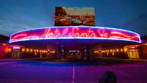 L'image montre l'enseigne au néon très éclairée de « l'Hôtel Santa Fe » à Disneyland Paris. Le panneau est dans des couleurs vives rouge et bleu, sur fond de ciel clair du soir.