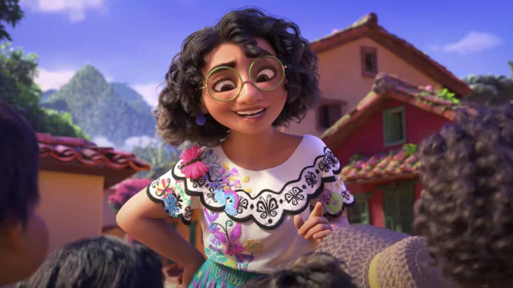 Une jeune fille animée aux cheveux bouclés et aux lunettes rondes sourit joyeusement dans une blouse colorée, entourée de personnages flous dans un décor de village animé rappelant un film de Disney comme Encanto.