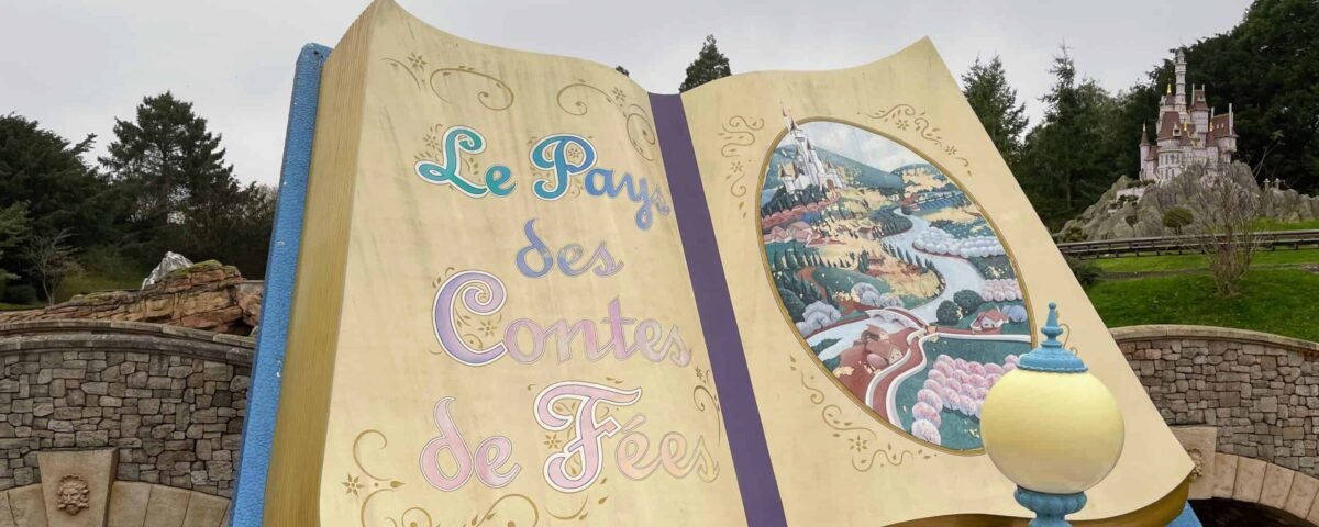Un grand livre de contes ouvert intitulé "le pays des contes de fées" à côté d'une promenade en bateau de conte de fées, avec une peinture colorée détaillée d'une scène de village sur les pages, et Raiponce