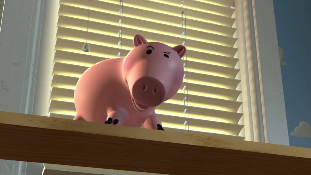 Une image animée en 3D d'un cochon rose de Toy Story de Pixar debout sur une poutre en bois, avec en toile de fond des stores laissant partiellement entrer la lumière du soleil. Deux ampoules suspendues sont visibles au-dessus.
