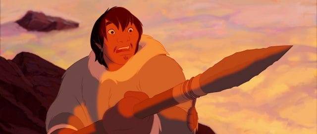 Un personnage animé dans un décor préhistorique, tenant une lance, semble surpris et déterminé sur un ciel orange éclairé par un coucher de soleil dans cette scène du film Disney "Frère des Ours.