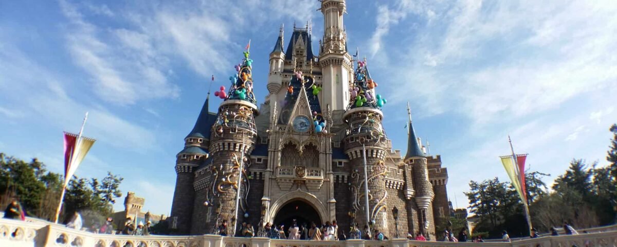 Plan large d'un château de conte de fées à Disneyland sous un ciel bleu clair, décoré de statues colorées de personnages Disney sur ses flèches et entouré d'arbres verts luxuriants.