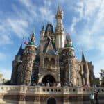 Plan large d'un château de conte de fées à Disneyland sous un ciel bleu clair, décoré de statues colorées de personnages Disney sur ses flèches et entouré d'arbres verts luxuriants.