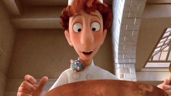 Un personnage animé, un jeune chef aux cheveux roux, sourit en tenant une cuillère en bois au-dessus d'une grande marmite de ratatouille, avec un petit rat bleu qui sort de sa veste de chef