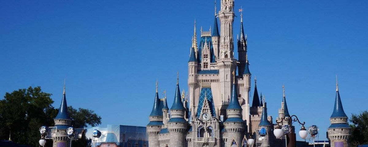 Château de Cendrillon à Disneyland, en Californie, par une journée ensoleillée. Le ciel est bleu clair et le château emblématique est décoré de lumières. Des gens sont visibles en train de profiter du parc au premier plan.