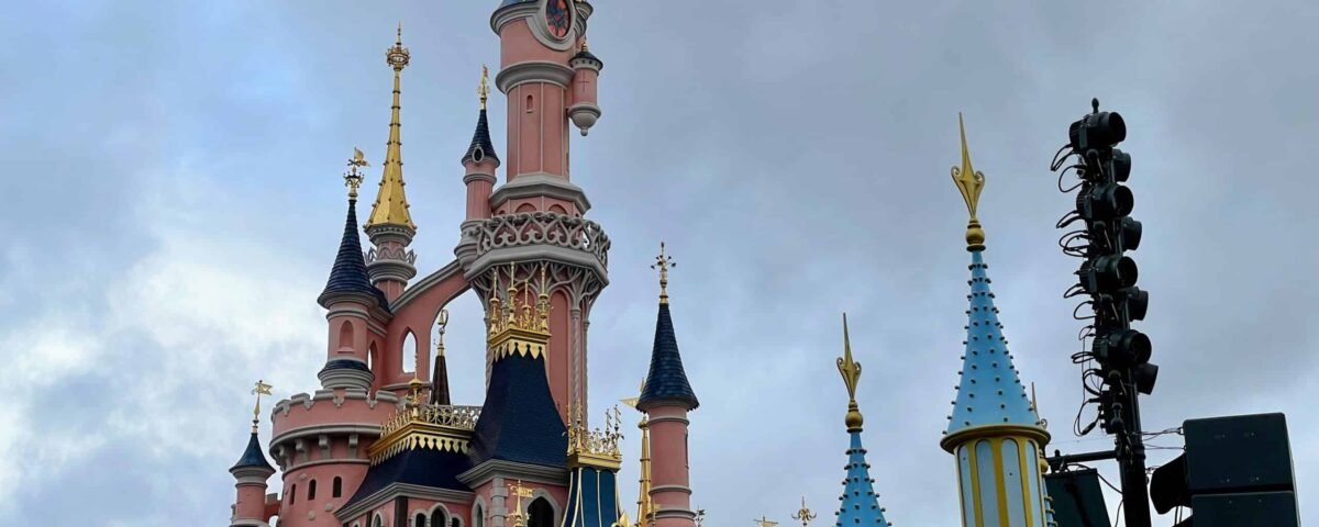 Le Château de la Belle au bois dormant à Disneyland Paris sous un ciel nuageux, avec ses flèches roses et bleues aux accents dorés, capture des moments magiques.