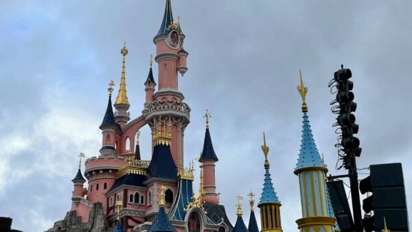 Le Château de la Belle au bois dormant à Disneyland Paris sous un ciel nuageux, avec ses flèches roses et bleues aux accents dorés, capture des moments magiques.