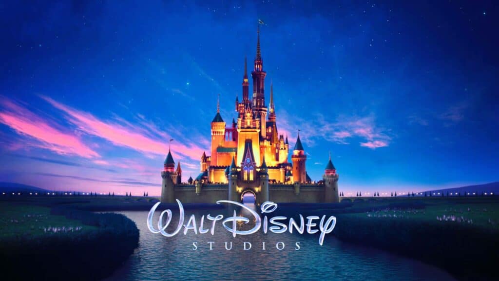 L'image montre le logo emblématique de Walt Disney Studios représentant un château de conte de fées avec des fenêtres éclairées au coucher du soleil sous un ciel crépusculaire, avec le texte « Walt Disney Studios » et un motif de puzzle dans le