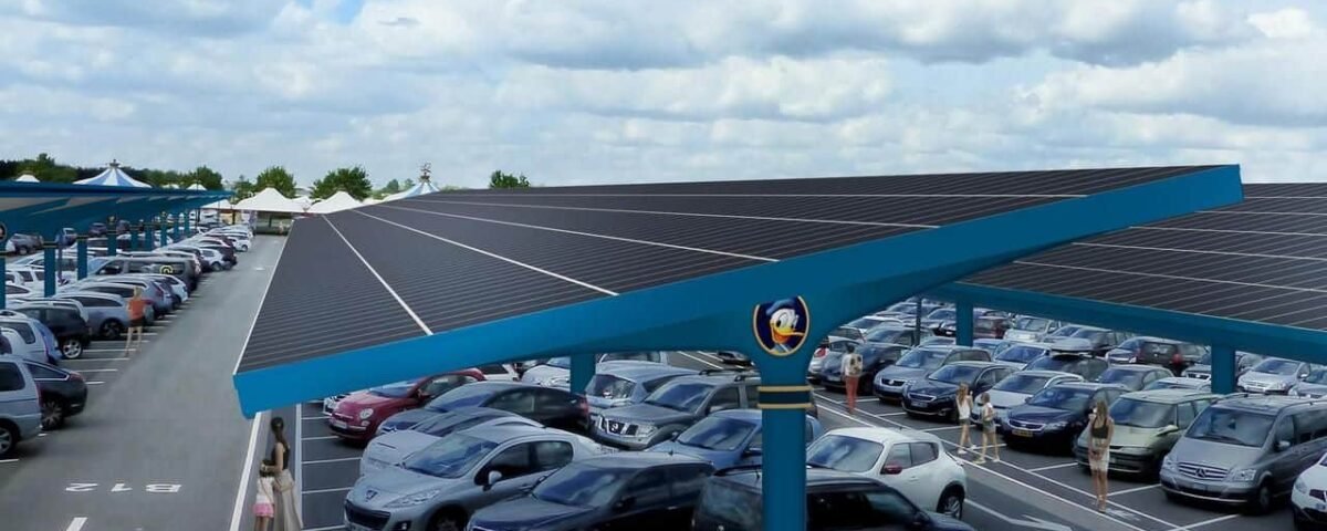 Un parking à Disneyland couvert par un grand auvent de panneaux solaires, ombrageant de nombreuses voitures garées et présentant un ciel ensoleillé avec des nuages épars au-dessus.