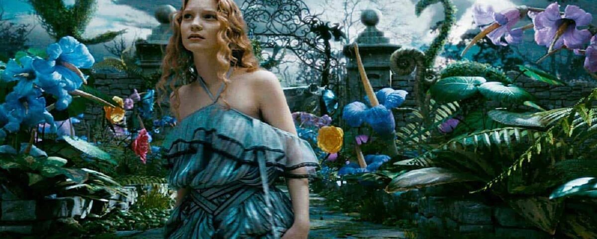 Alice, une jeune femme vêtue d'une robe fluide bleue et grise, se tient dans un jardin fantastique et vibrant avec des fleurs colorées surdimensionnées et une porte en métal ornée en arrière-plan, rappelant une scène.