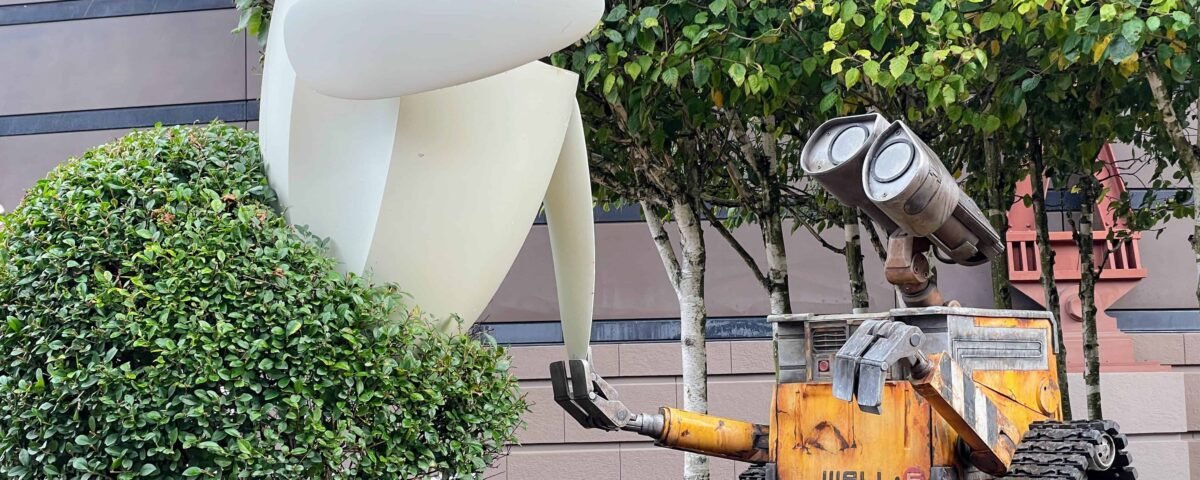 Un grand modèle du robot Eve du film "wall-e" debout à côté d'un modèle tout aussi grand de wall-e lui-même, entouré d'arbustes et adossé à un bâtiment.