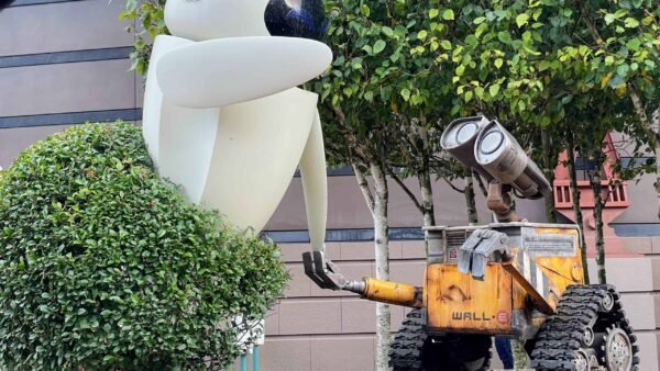 Un grand modèle du robot Eve du film "wall-e" debout à côté d'un modèle tout aussi grand de wall-e lui-même, entouré d'arbustes et adossé à un bâtiment.