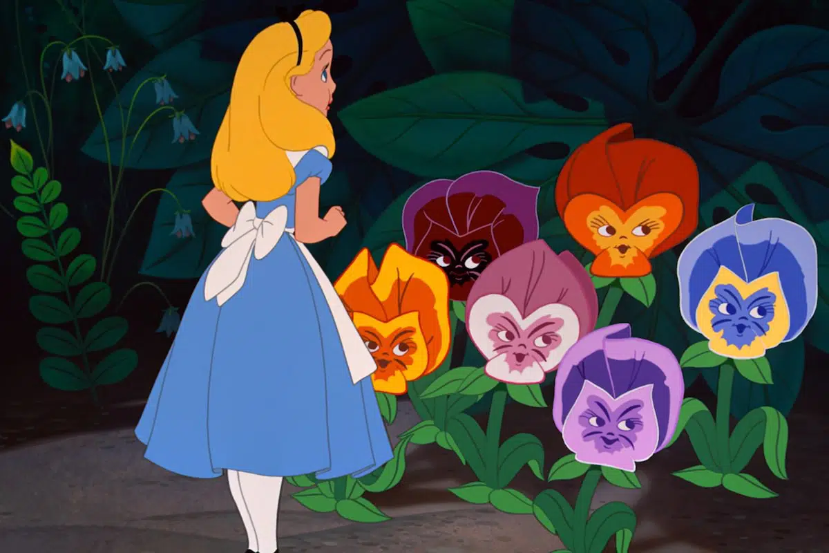 Alice de "Alice au pays des merveilles" regarde avec curiosité un groupe de fleurs colorées et animées aux visages expressifs, sur un fond sombre et feuillu.