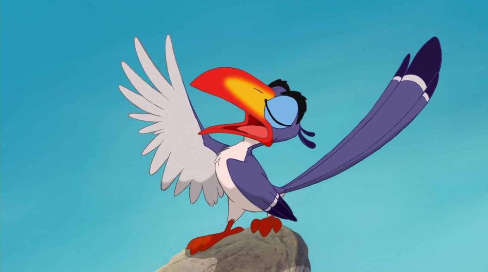 Un toucan animé coloré avec des ailes blanches et violettes et des pattes rouges, prenant une pose ludique sur un rocher, sur un fond bleu ciel, rappelant les Personnages Le Roi Lion.