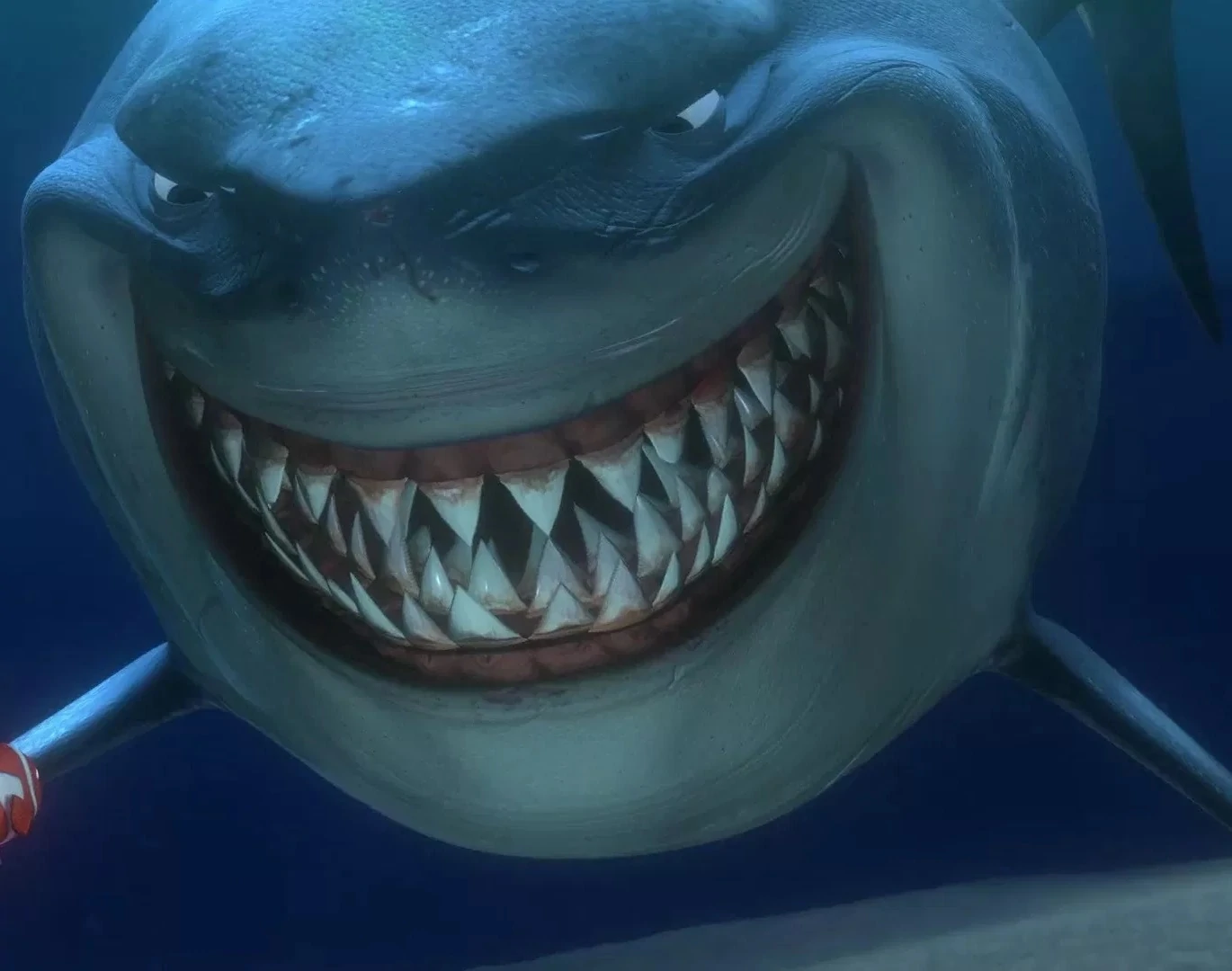 Un requin animé avec un large sourire, montrant des dents pointues, et un harpon visible au premier plan sous l'eau bleue de l'océan, rappelant "Le Monde de Nemo".
