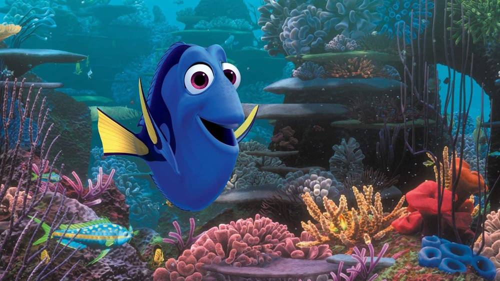 Image animée de Dory, un poisson bleu et jaune du « Monde de Nemo », nageant joyeusement près d'un récif de corail vibrant avec diverses plantes sous-marines colorées et une vie marine.